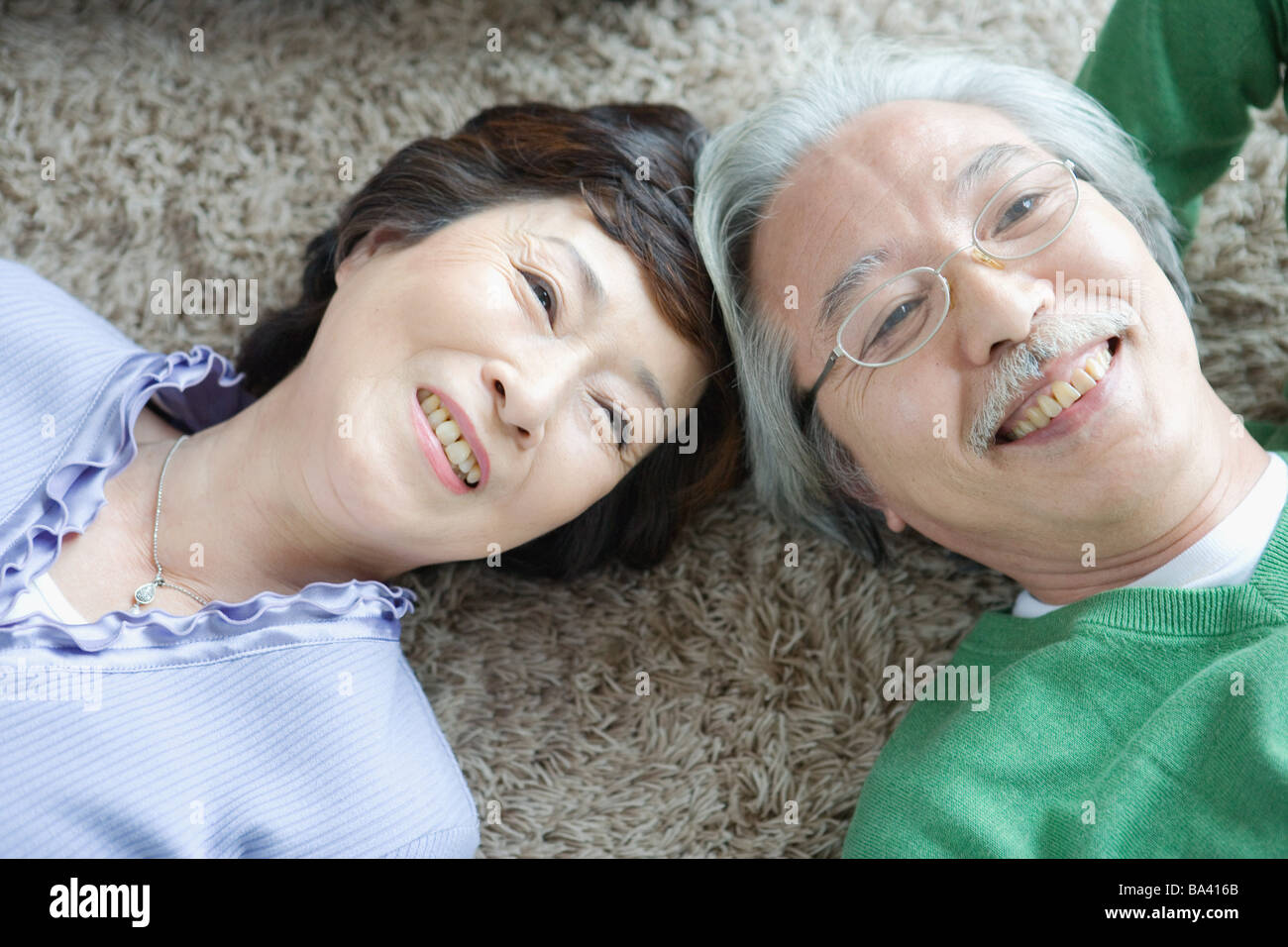 Senior couple lying head to head on carpet Stock Photo