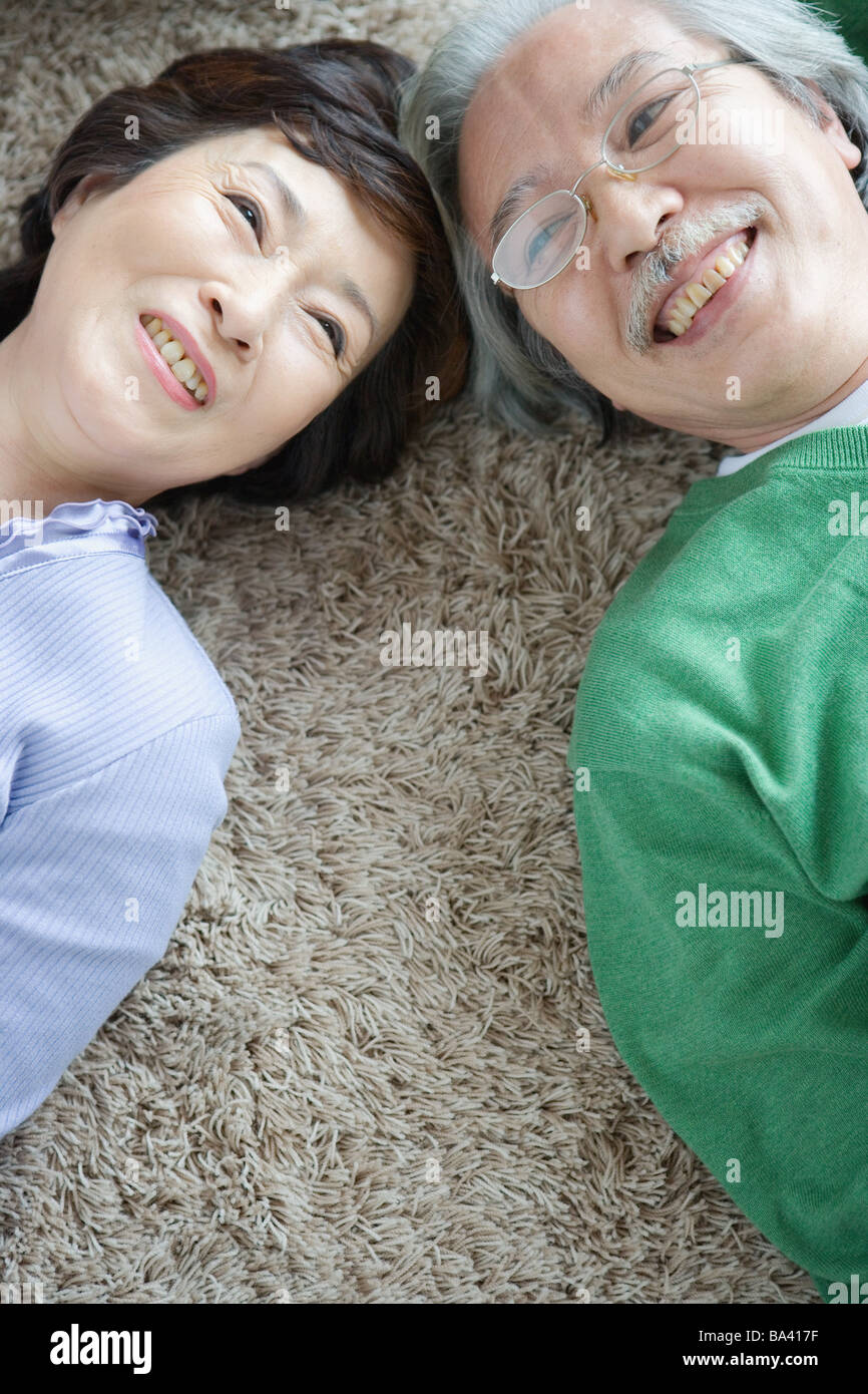 Senior couple lying head to head on carpet Stock Photo