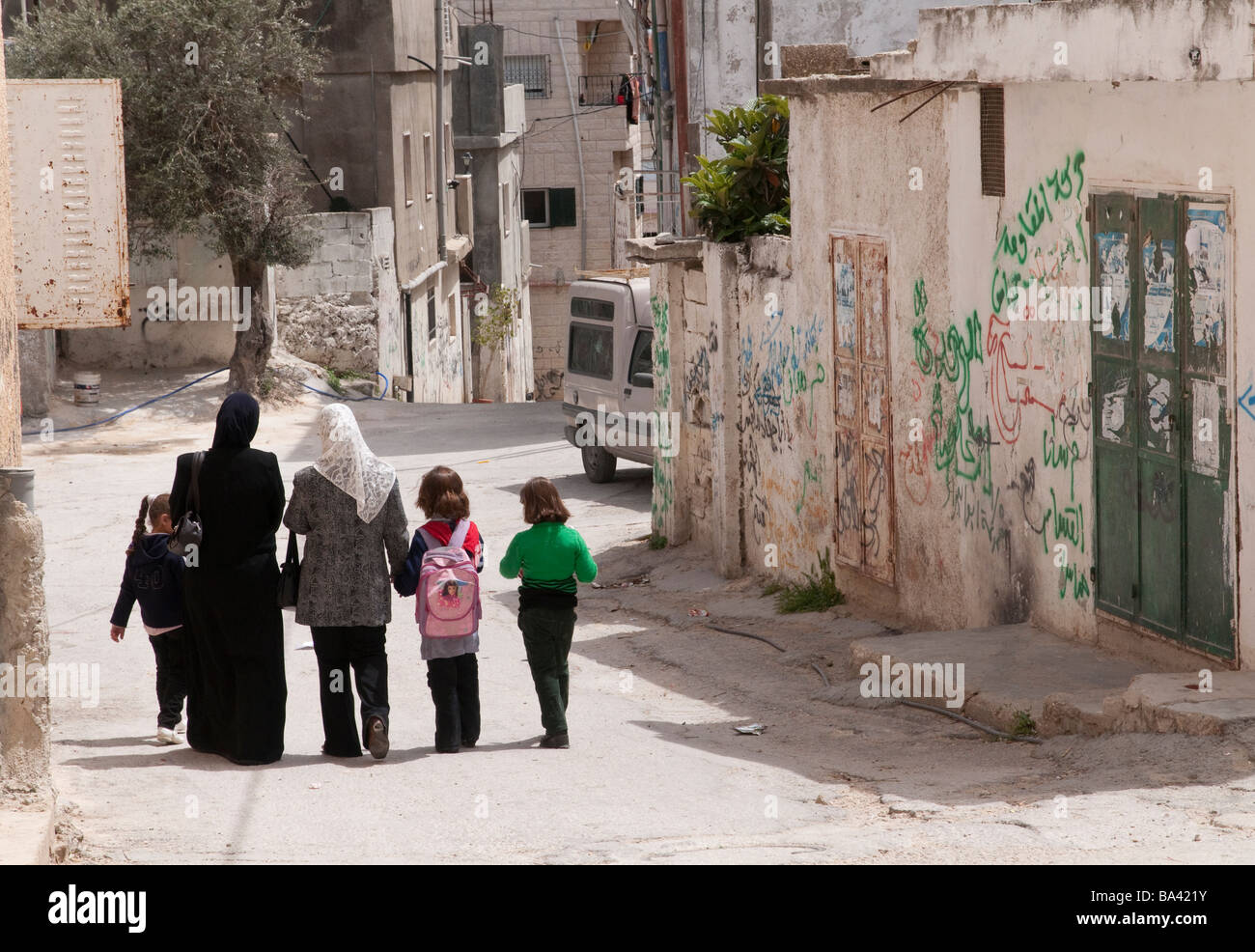 Palestinian Authority Bethlehem Aida refugee camp women and children walking passed walls graffitis in the street Stock Photo