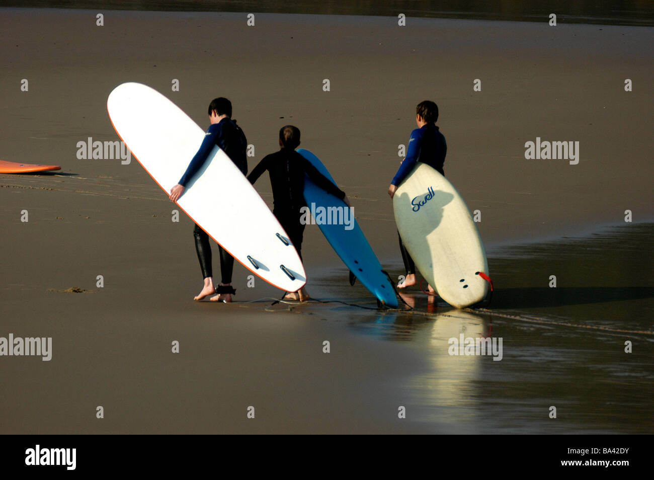 teenage boys carrying there surfboards up a sandy beach Stock Photo Alamy