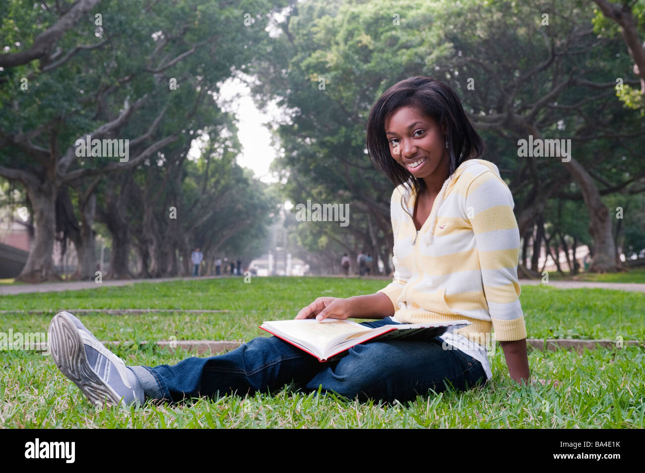 Young Woman Sitting In Park Reading A Book Stock Photo - Alamy