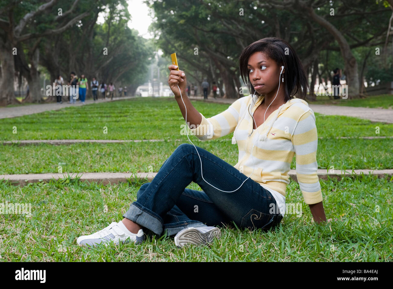 Young Woman Sitting In Park Listening To Music On Mp3 Player Stock Photo