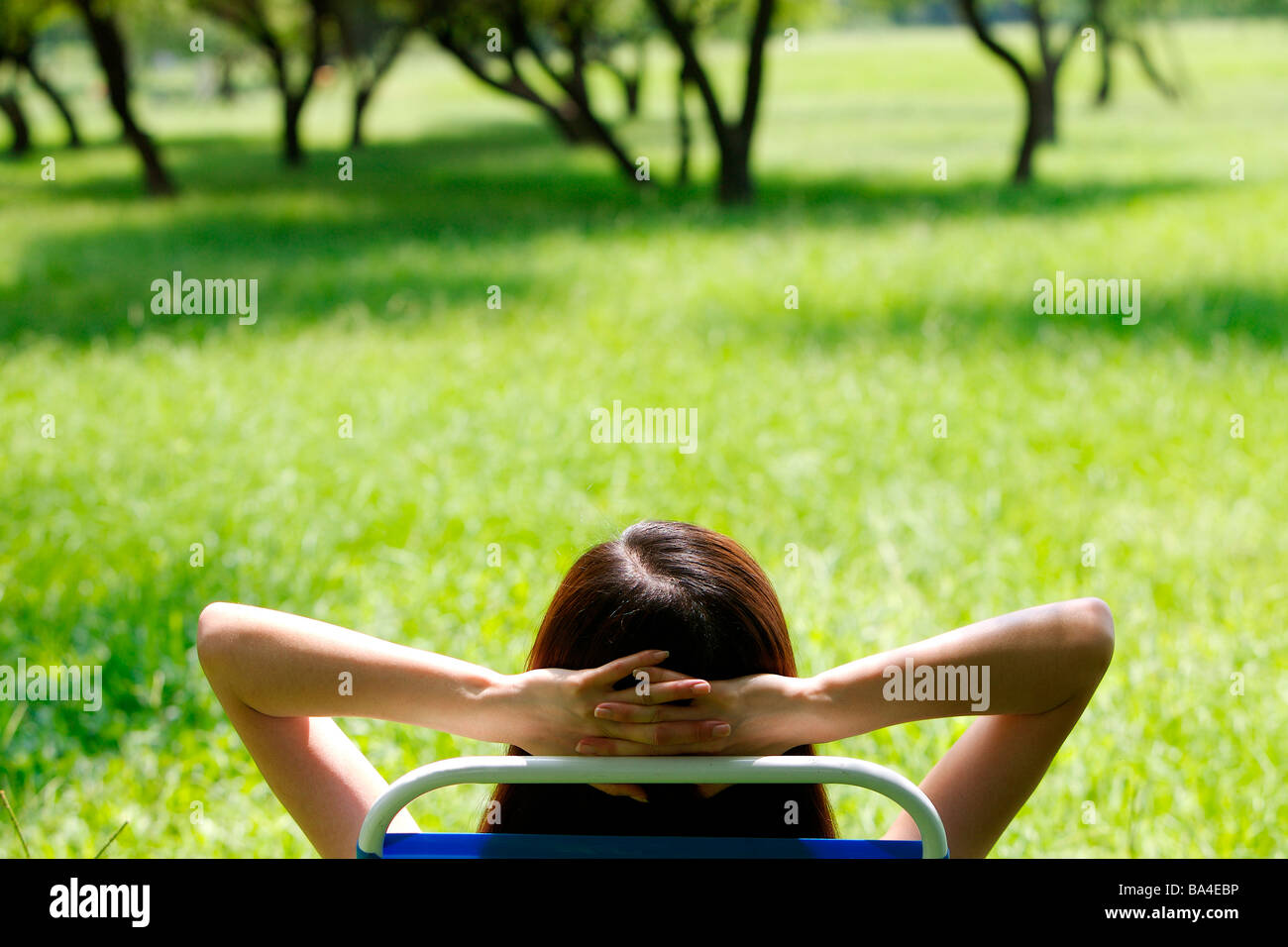 Rear view of young woman lying on chair hands under head Stock Photo
