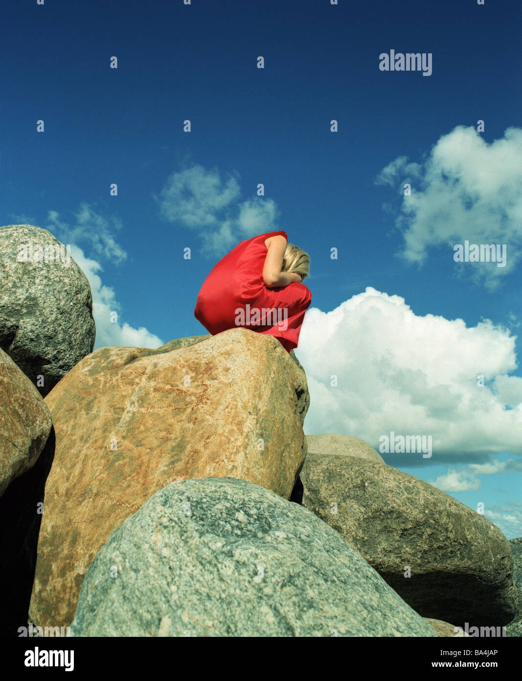 Boulders woman dress red crouches rocks hide face cloud-heavens stones people young blond crouch cries however leaves knocked Stock Photo