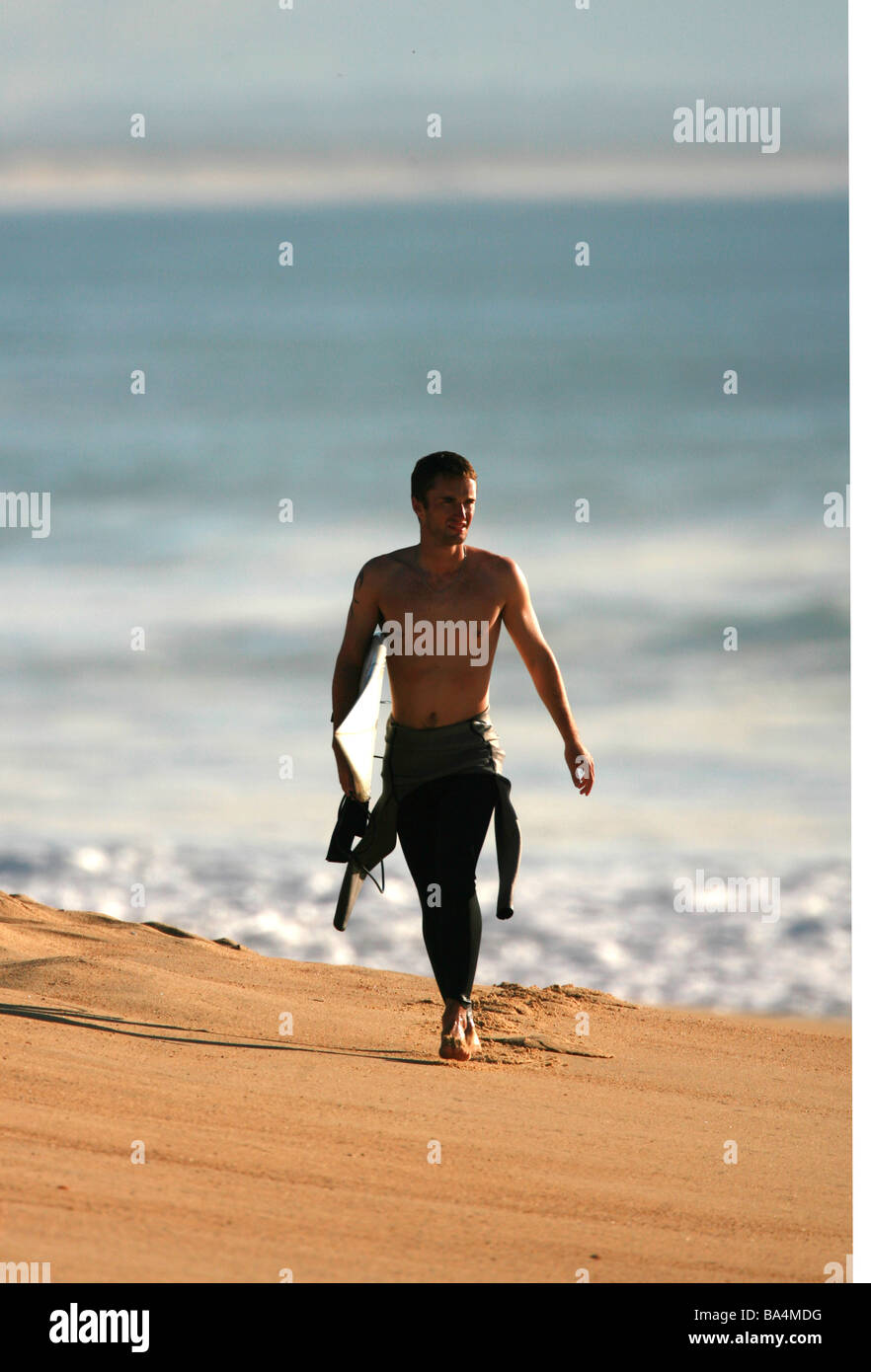 A Surfer walking along the beach with his surfboard Stock Photo - Alamy