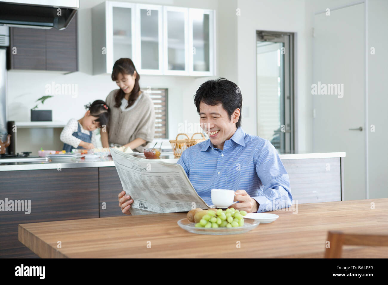 Father reading newspaper with family in background Stock Photo