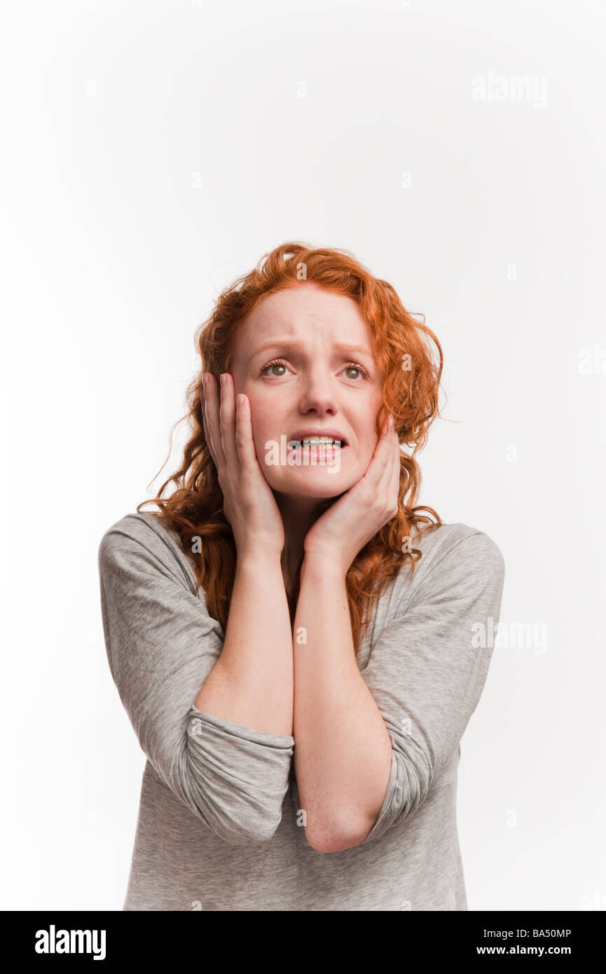 An anxious worried stressed long red haired young woman girl in studio holding her head in her hands Stock Photo
