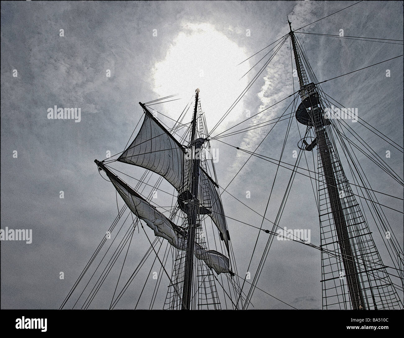 tall-ship tall-ships two masts and unfurled sail against bright sun and gray clouds, done in drawing detail style, ropes, lines Stock Photo