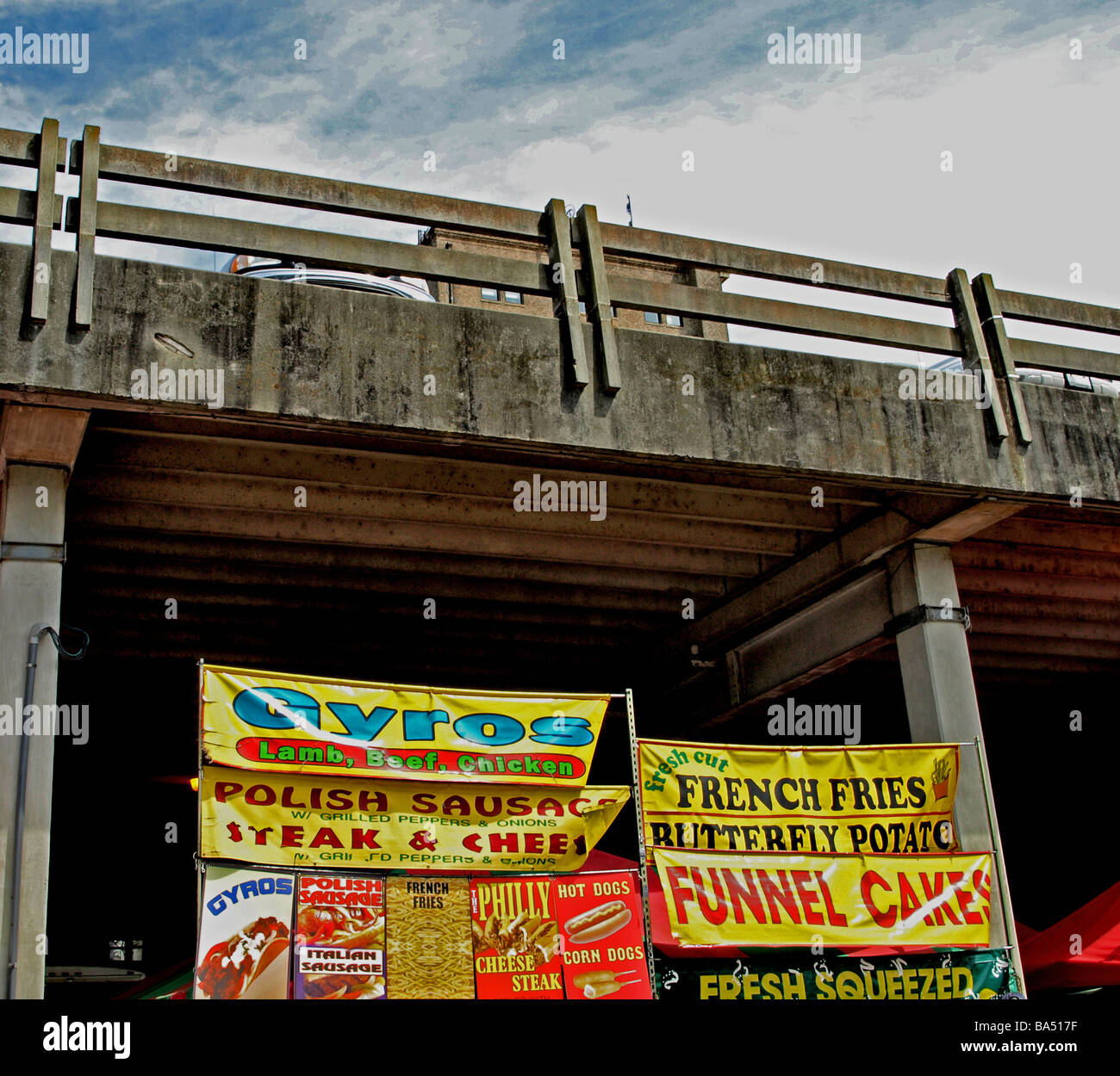 carnival festival food stand signs for funnel cakes hot dogs framed by parking garage and sky Stock Photo
