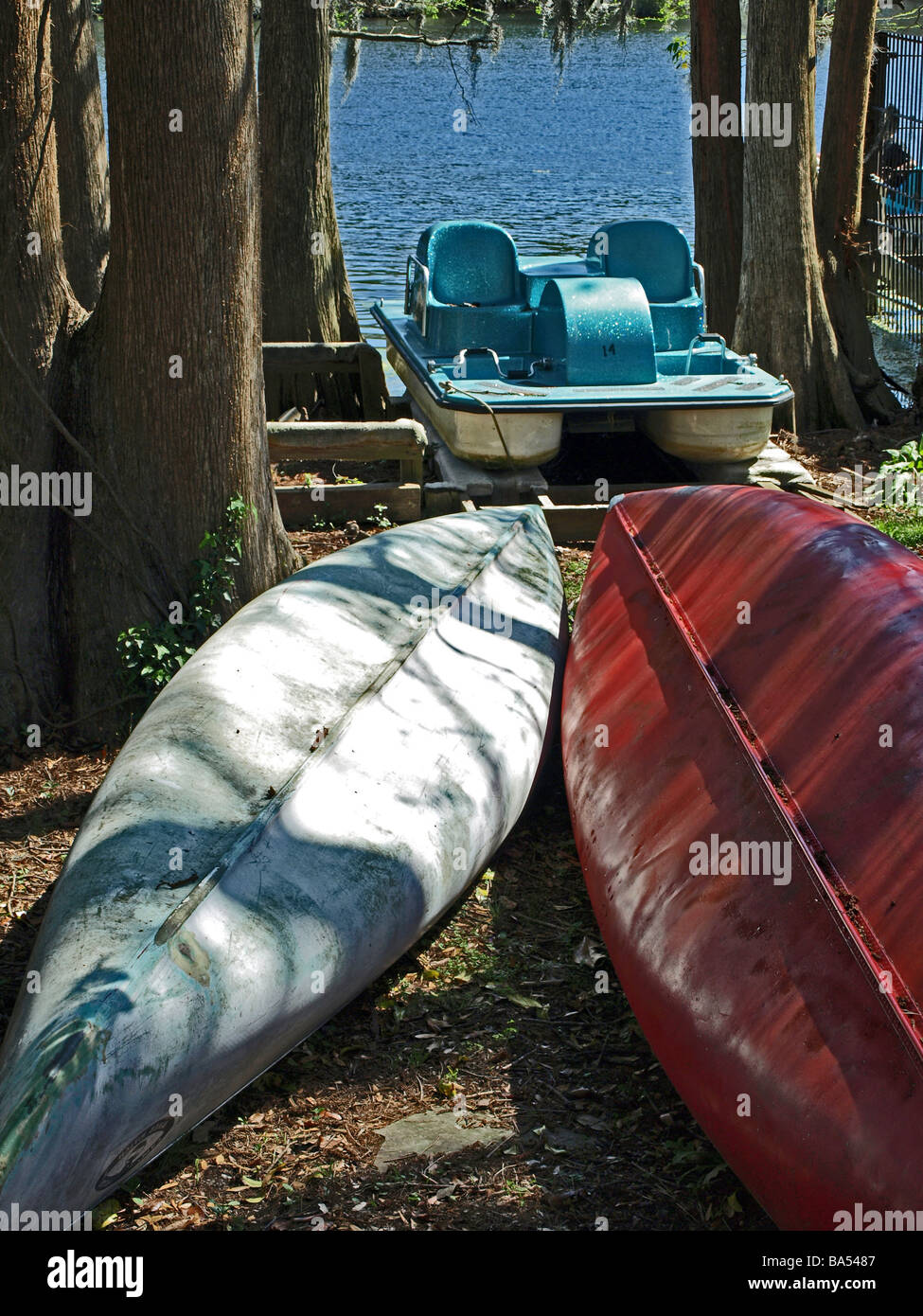 two canoes on shore upside down with the lake in the background and also a peddle wheel boat surrounded by trees Stock Photo