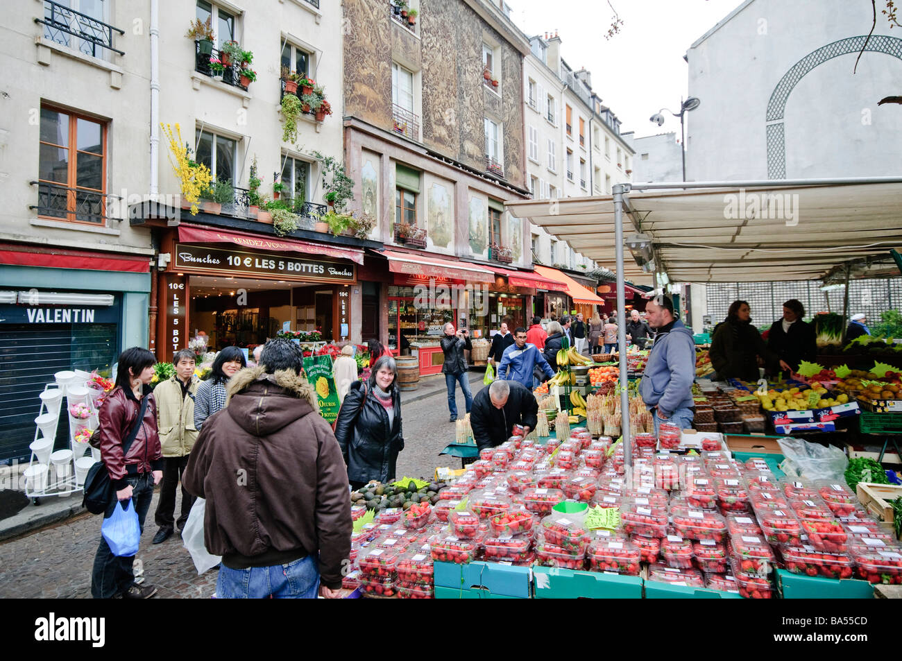 Rue Mouffetard Market Fresh Produce Shoppers Paris France // PARIS, France — The Rue Mouffetard Market, a vibrant fresh produce market, is located in the 5th arrondissement of Paris. Stalls brim with colorful fruits, vegetables, and other local goods, creating a lively atmosphere. Shoppers and vendors engage in animated exchanges throughout the historic street. Rue Mouffetard is renowned as one of Paris's oldest and most charming market streets. It remains a popular destination, drawing both residents and visitors seeking an authentic Parisian experience. Stock Photo