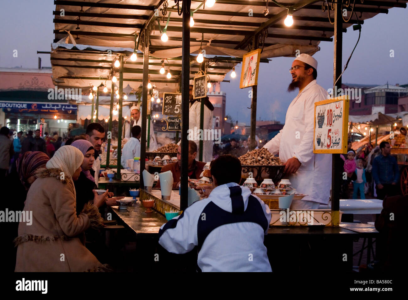 Stallholder selling soups seen at dusk amongst the many restaurant stalls that offer food to locals and tourists, Marrakech Stock Photo