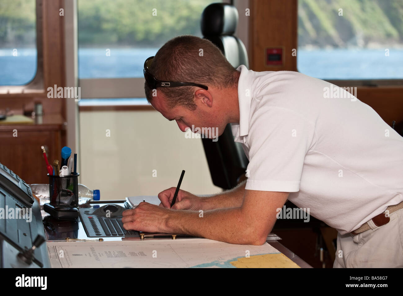 Chief Officer writing up the log book at the chart table aboard superyacht 'Big Aron' Stock Photo
