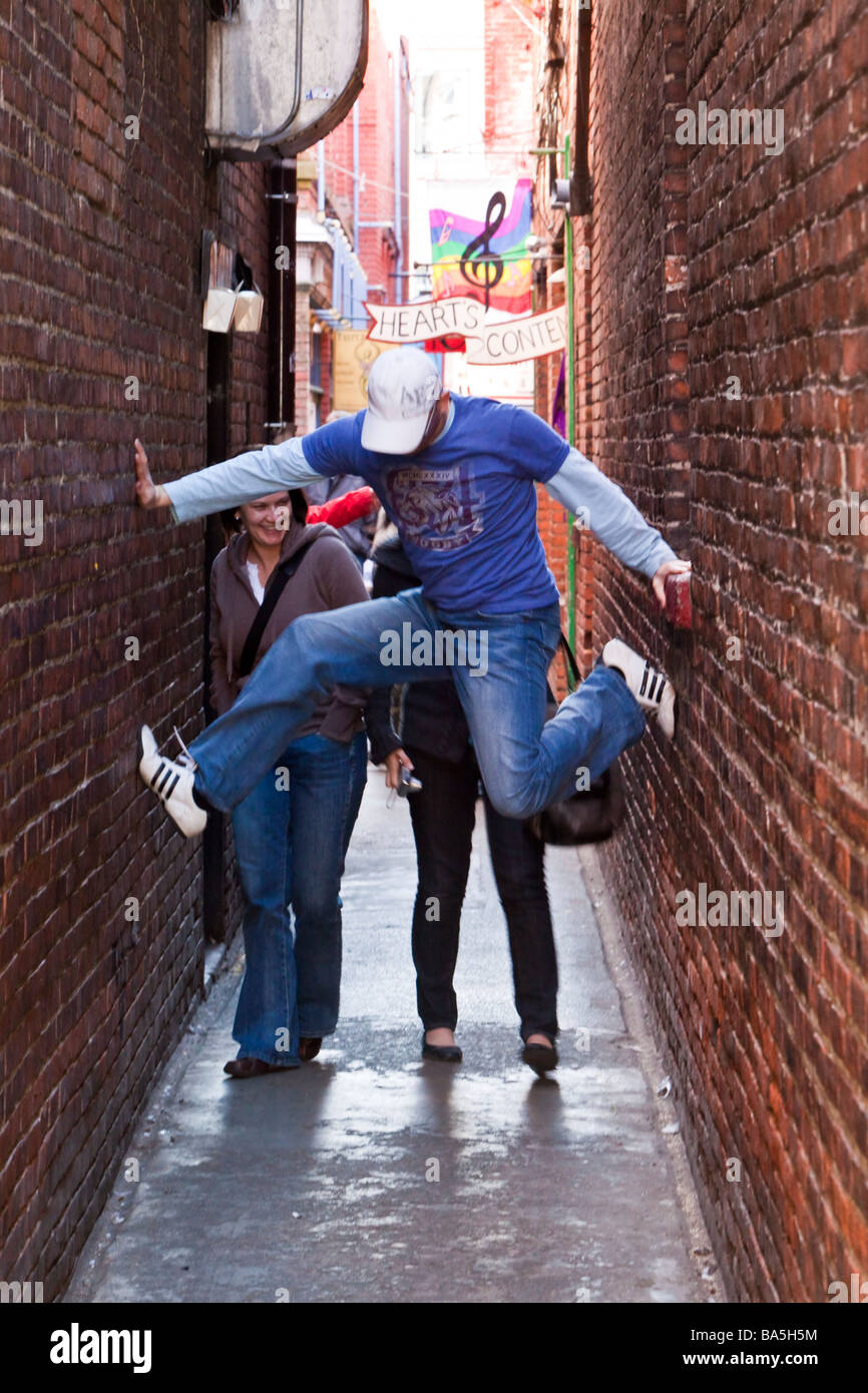 Man performing a split between the walls of a narrow street Fan Tan Alley in Chinatown Victoria BC Canada Stock Photo