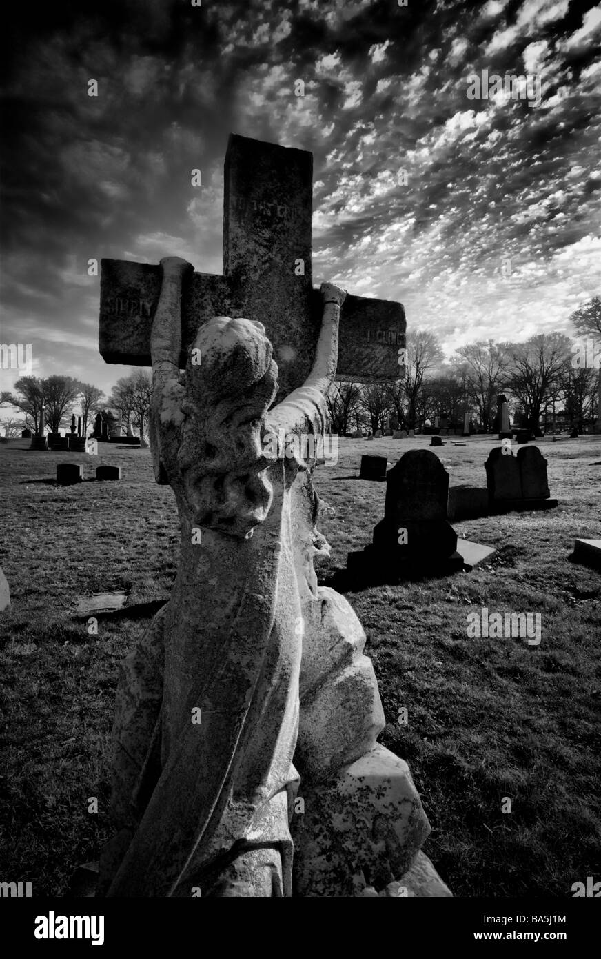 A statue of a girl clinging to a cross against a dramatic sky. This emotional tombstone is in Allegheny Cemetery, Pittsburgh, PA Stock Photo