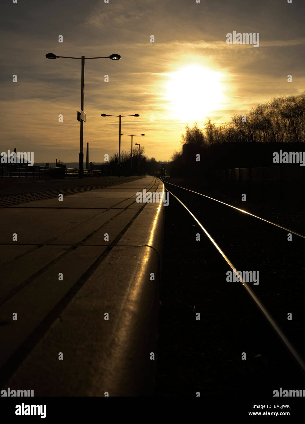 Looking along a railway station platform into the setting sun Stock Photo