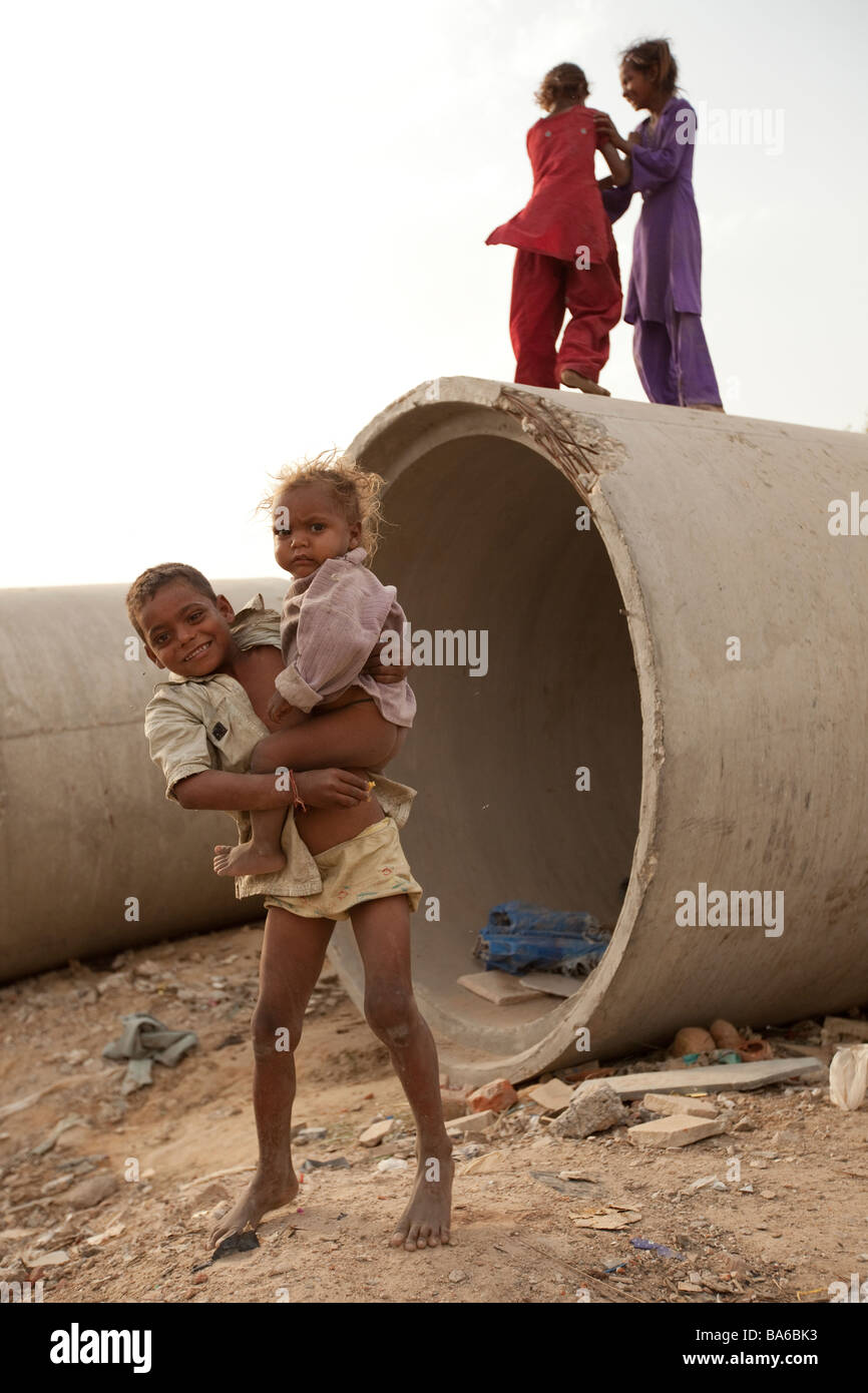An Indian boy plays with his sisters among sewerage pipes opposite  construction zone in Gurgaon a satellite city south of Delhi Stock Photo