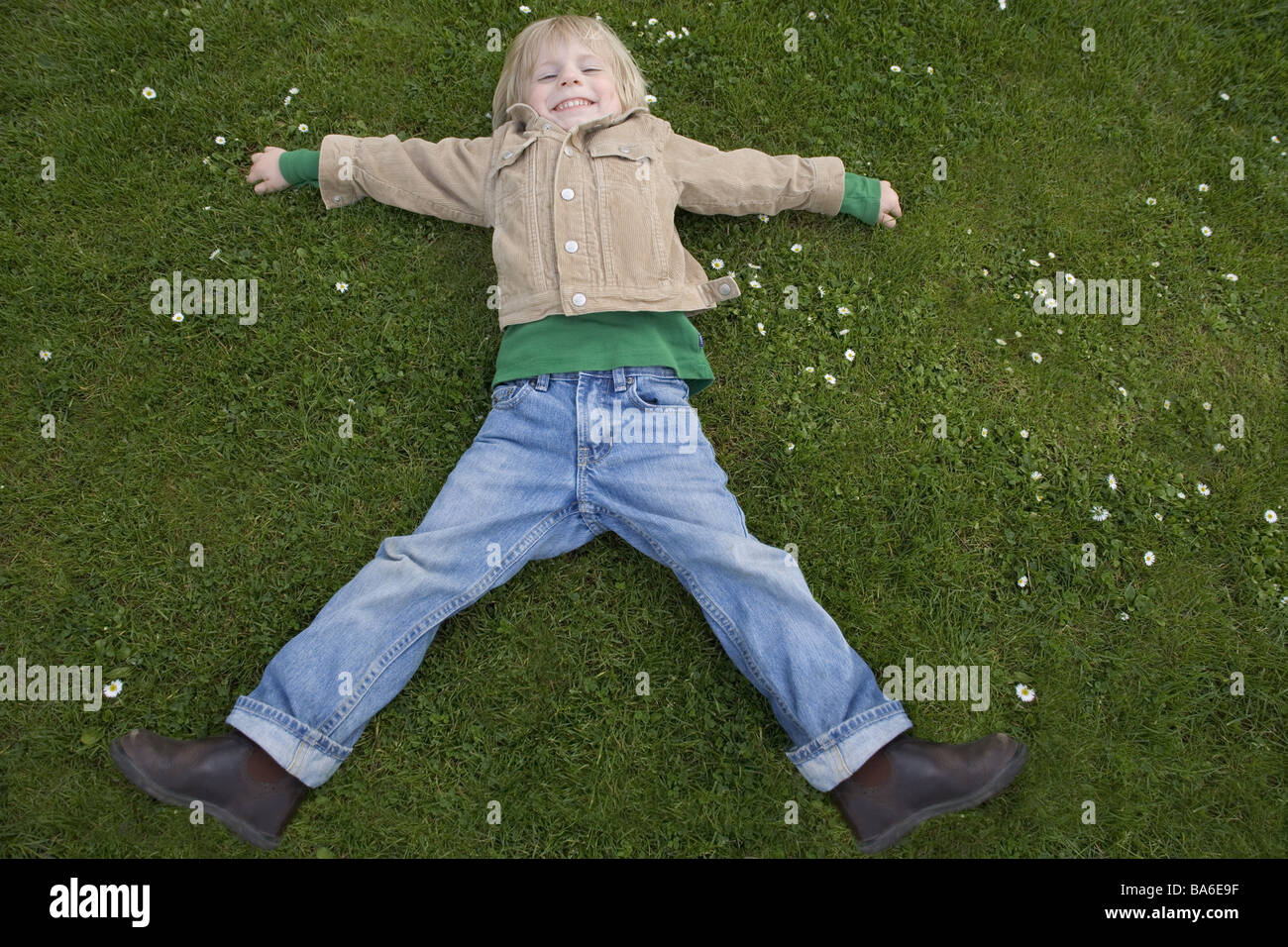 Give birth meadow lies poor legs stretched out laughs child blond 3-6 years series childhood freely park garden game plays Stock Photo