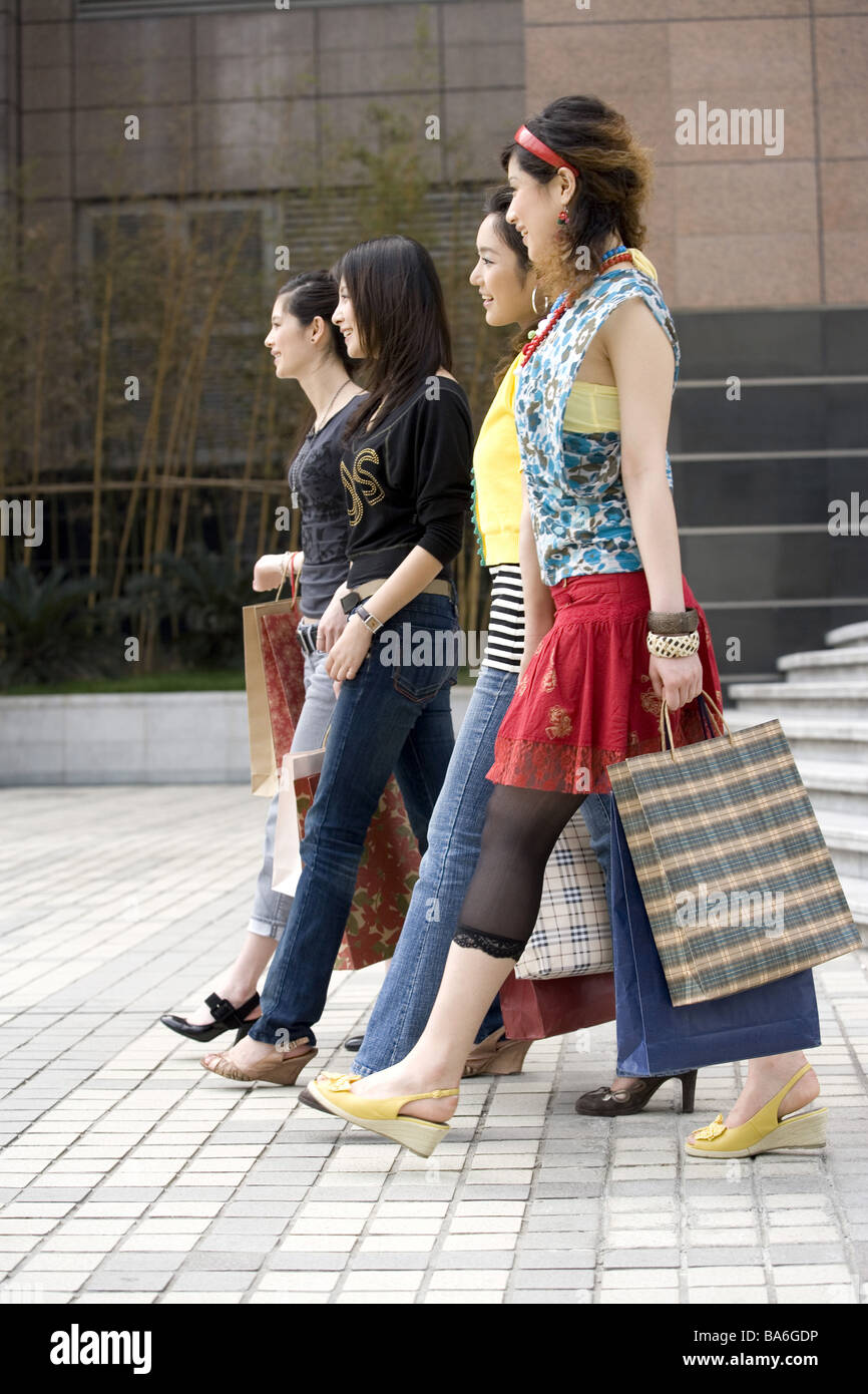 Four young women walking side by side with shopping bags Stock Photo ...