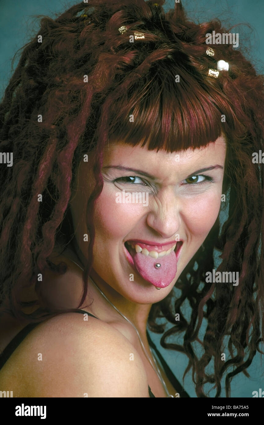 Caucasian woman with red hair,  tattoos and tongue piercing sticking out tongue as she makes a silly face, showing piercing. Stock Photo