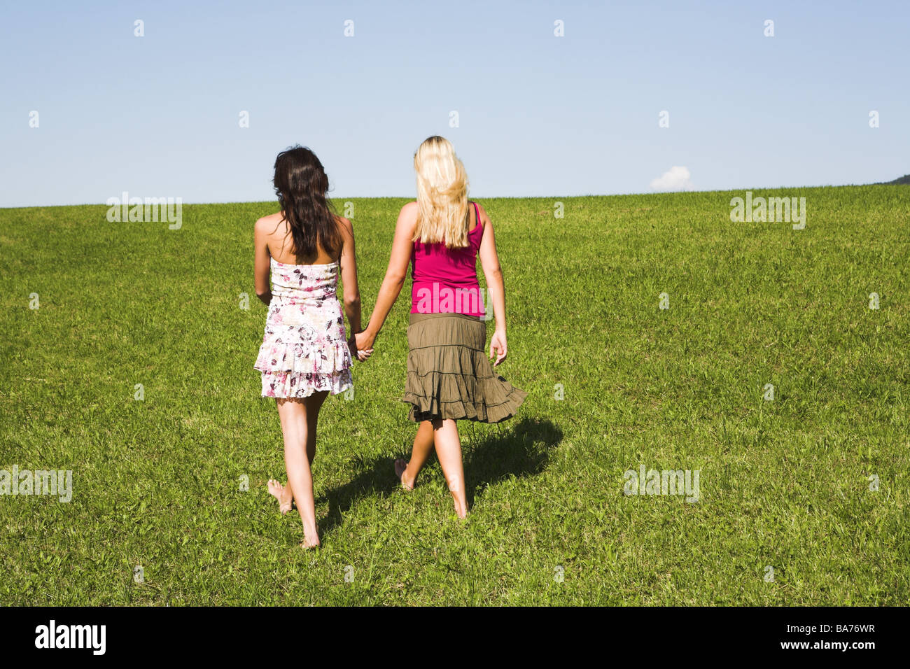 Teenagers girls barefoot walk meadow hand in hand back-opinion series people 18-19 years friends long-haired hair-color Stock Photo