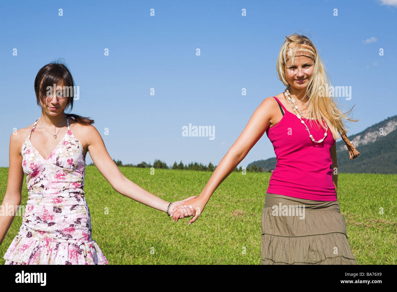 Teenagers girls walk meadow cheerfully hand in hand detail series people 18-19 years friends long-haired hair-color deceased Stock Photo