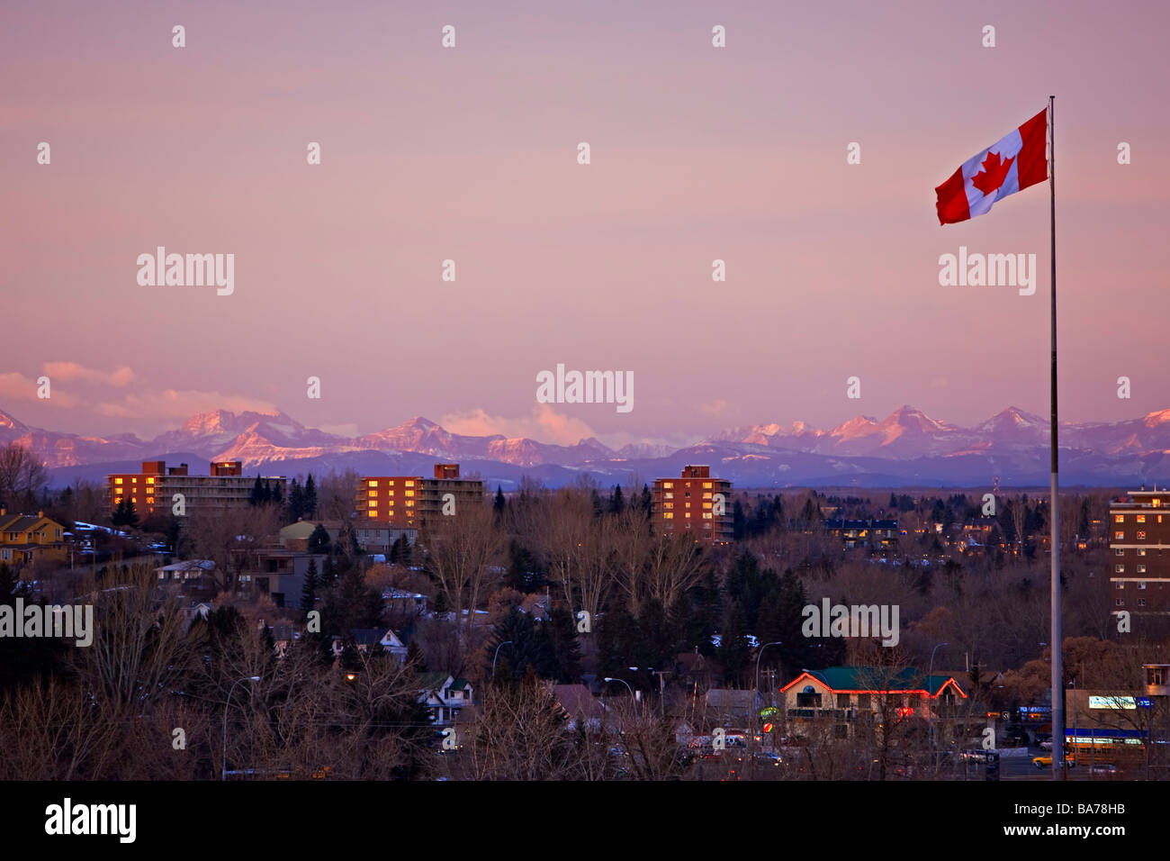 Canadian flag flying from a flag pole in the city of Calgary with the Canadian Rocky Mountains of Banff National Park. Stock Photo