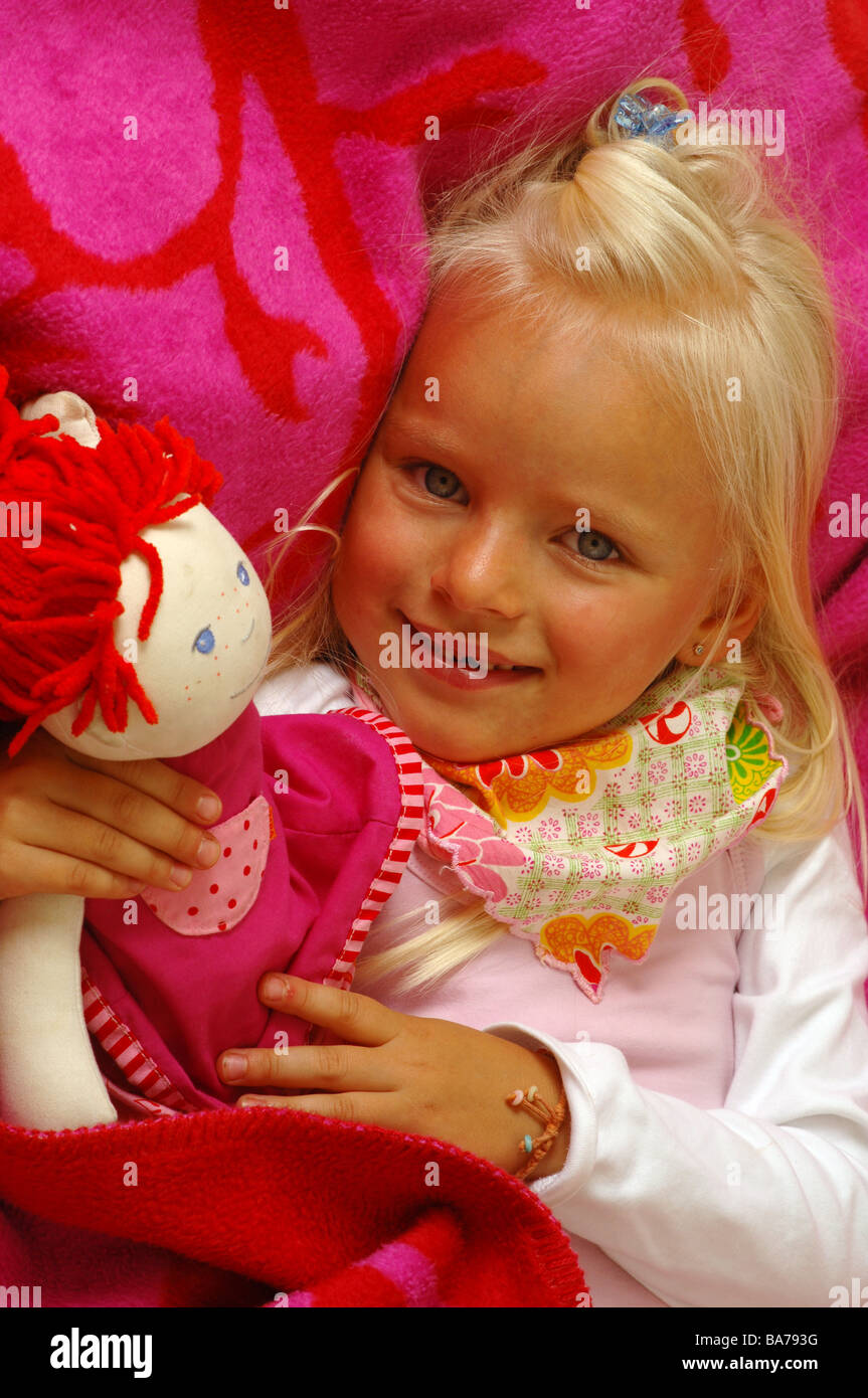 Girls smiles doll cuddles lies portrait series people 5 years child-portrait child toddler blond gaze camera scarf childhood Stock Photo
