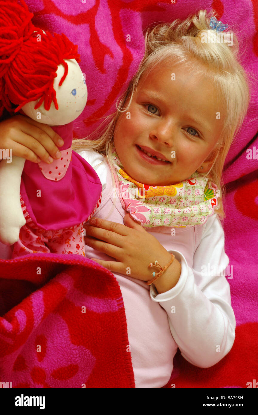 Girls smiles doll cuddles lies portrait series people 5 years child-portrait child toddler blond gaze camera scarf childhood Stock Photo