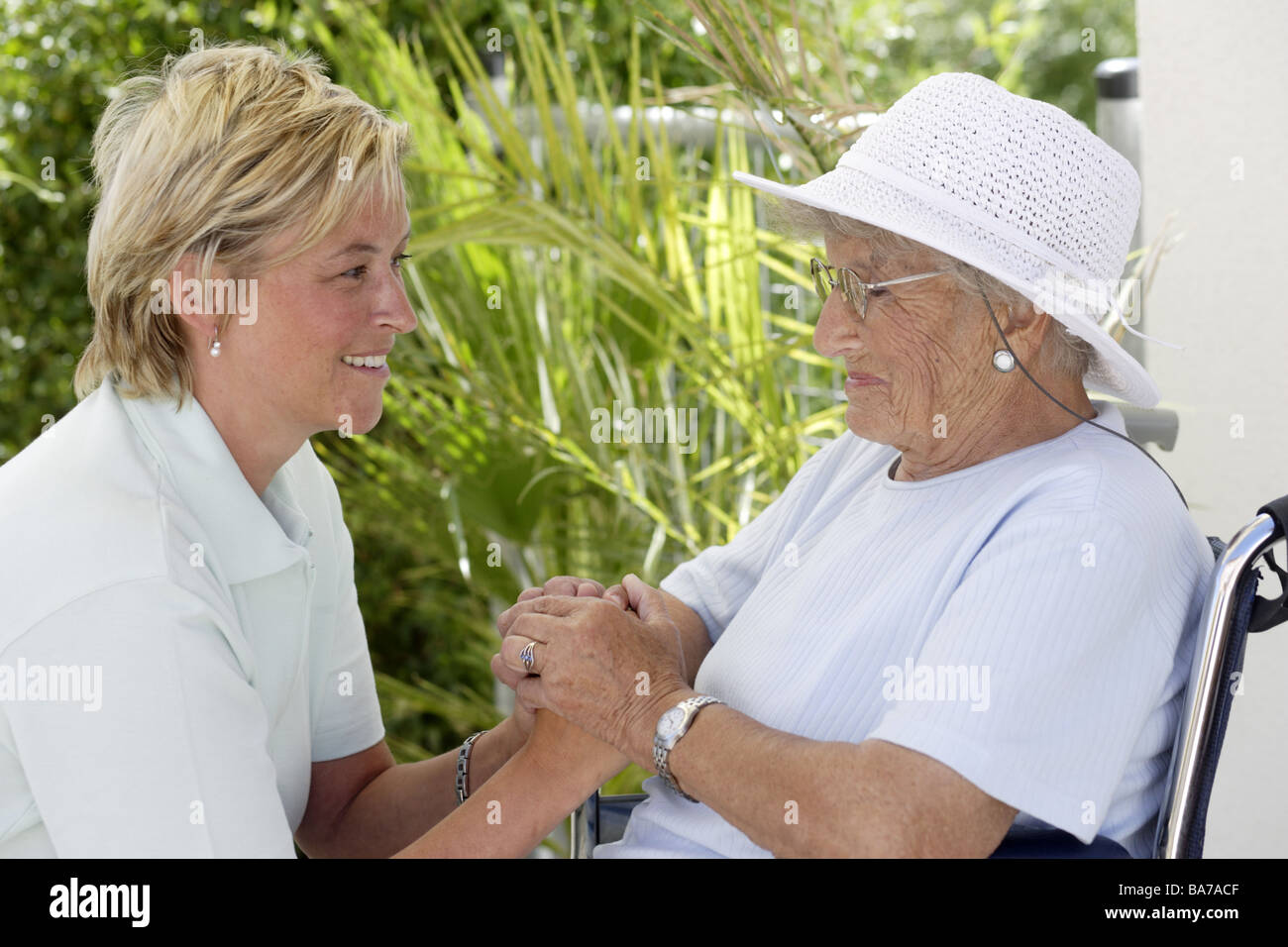 Senior-home terrace senior wheelchair keeper laughs cheerfully series people seniors woman 70-80 years hat sunhat keeper 30-40 Stock Photo