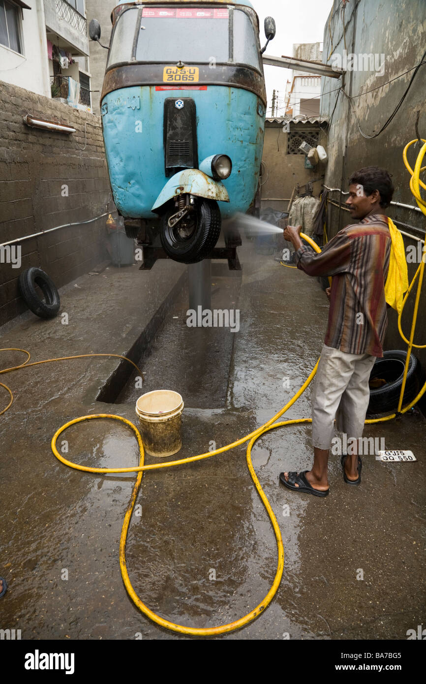 Indian man washing a rickshaw with a hose pipe in Surat, India Stock