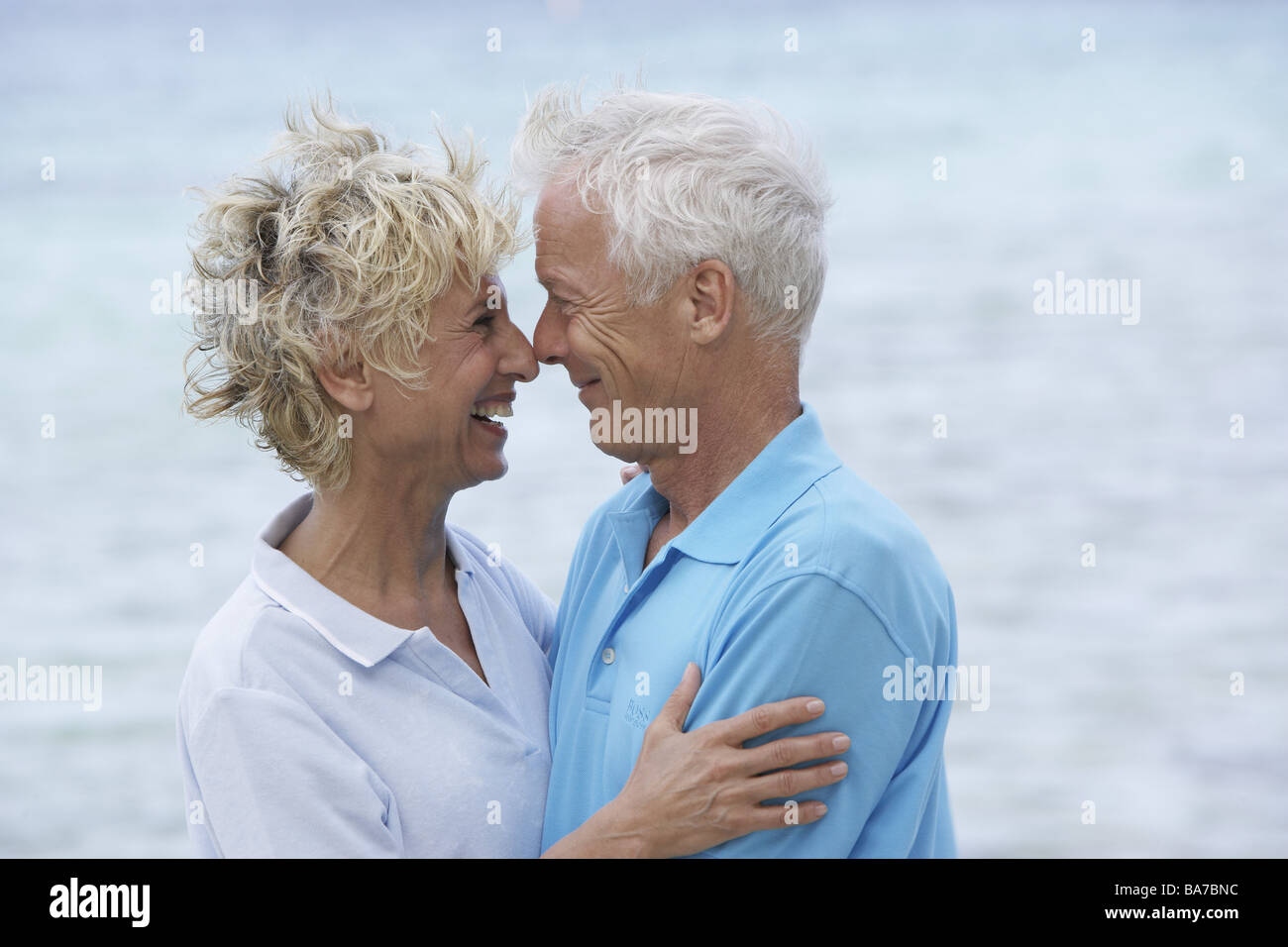 Sandy beach senior-pair embrace smiles cheerfully side-portrait series people 50-60 years 60-70 years seniors pair gaze-contact Stock Photo