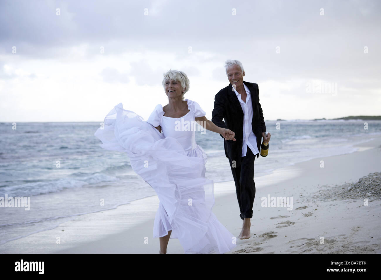 Sandy beach wedding-pair champagne-bottle sand runs cheerfully detail  series people 50-60 years 60-70 years seniors pair Stock Photo - Alamy