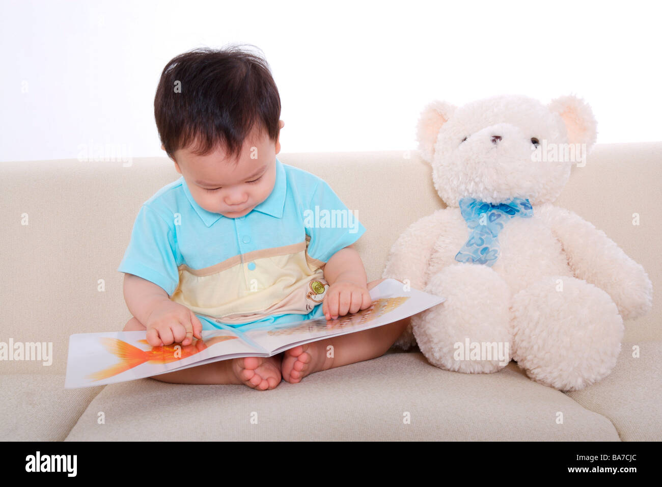 Baby boy sitting on sofa looking at picture book Stock Photo - Alamy