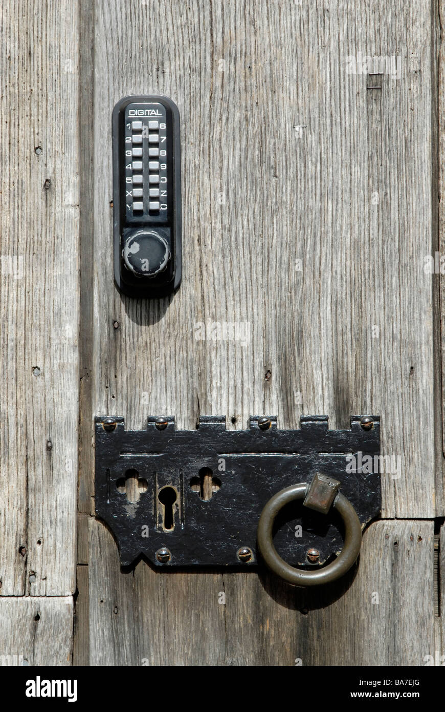 Double security: New digital push button pad lock alongside ancient key operated lock on weathered church door, Winchester Stock Photo