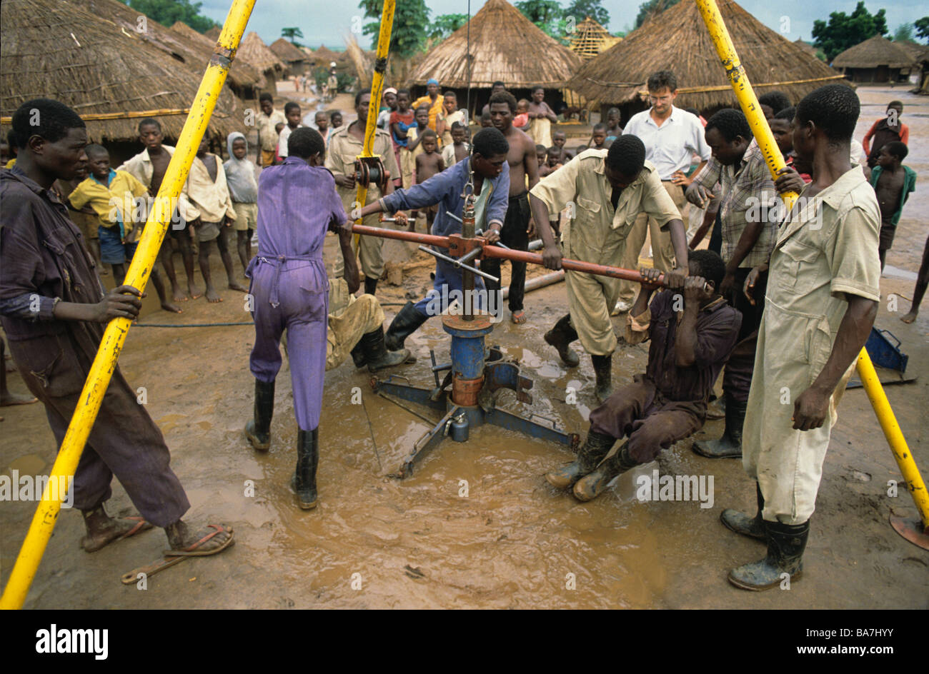 Children crowd around workers boring a well in Malawian village after floods Stock Photo