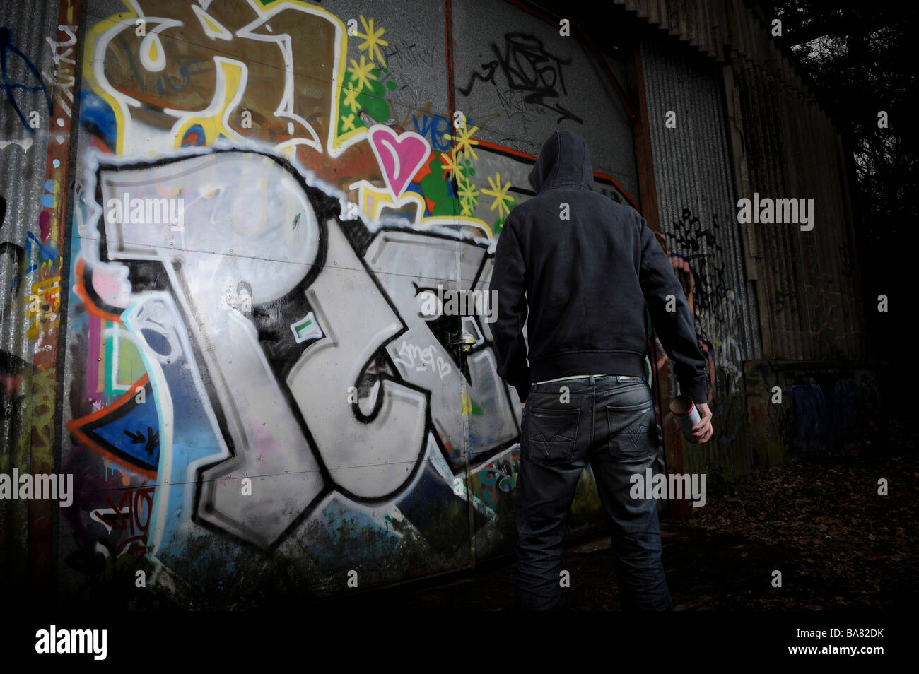 A person in dark clothing standing near a graffitied surface Stock Photo