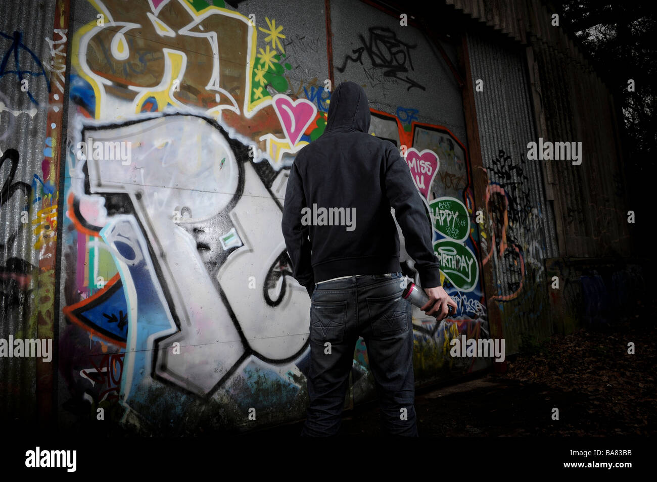 Person in dark clothing standing in front of a graffittied surface Stock Photo