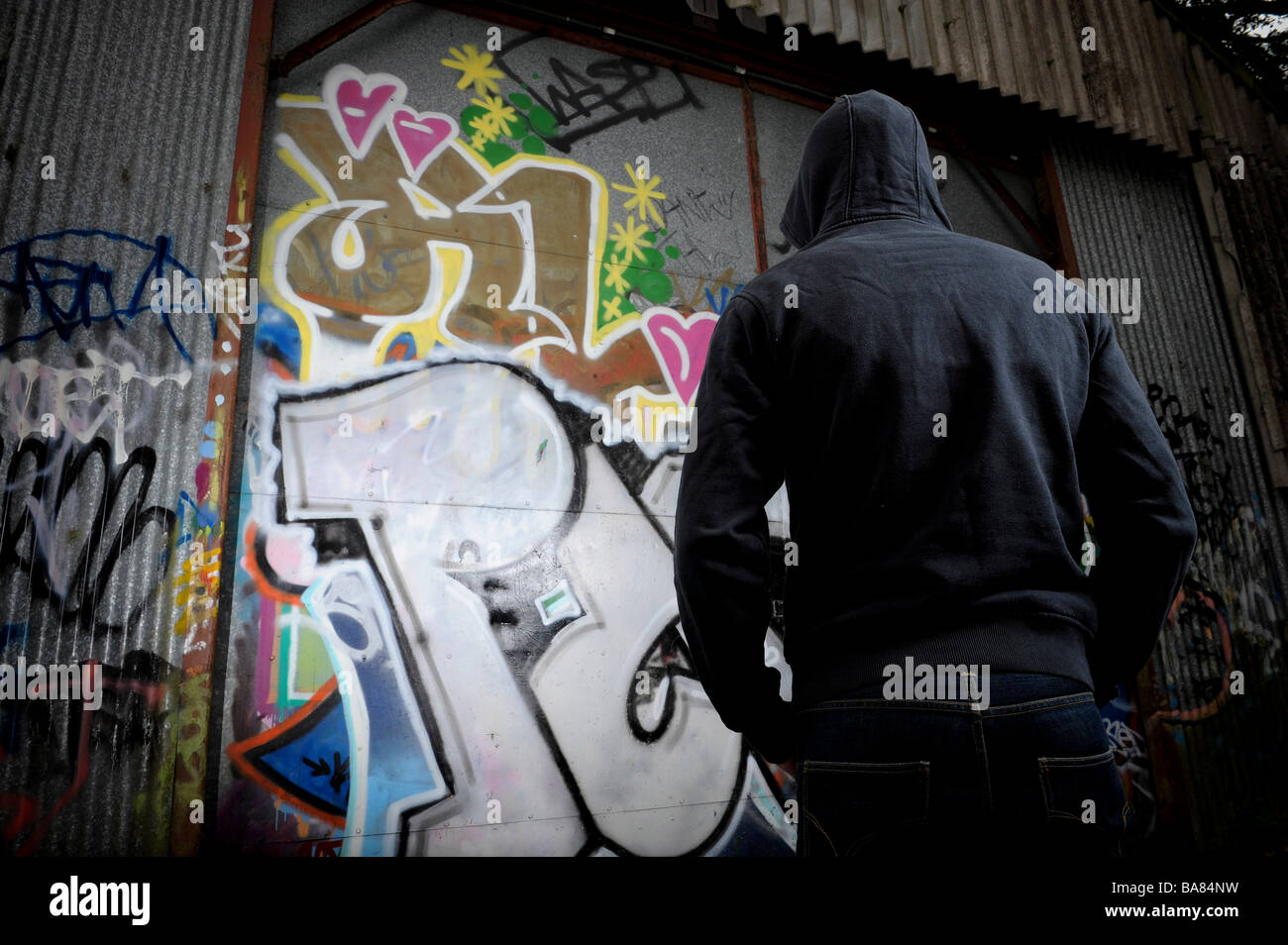 Person in dark clothing standing in front of a graffittied surface Stock Photo
