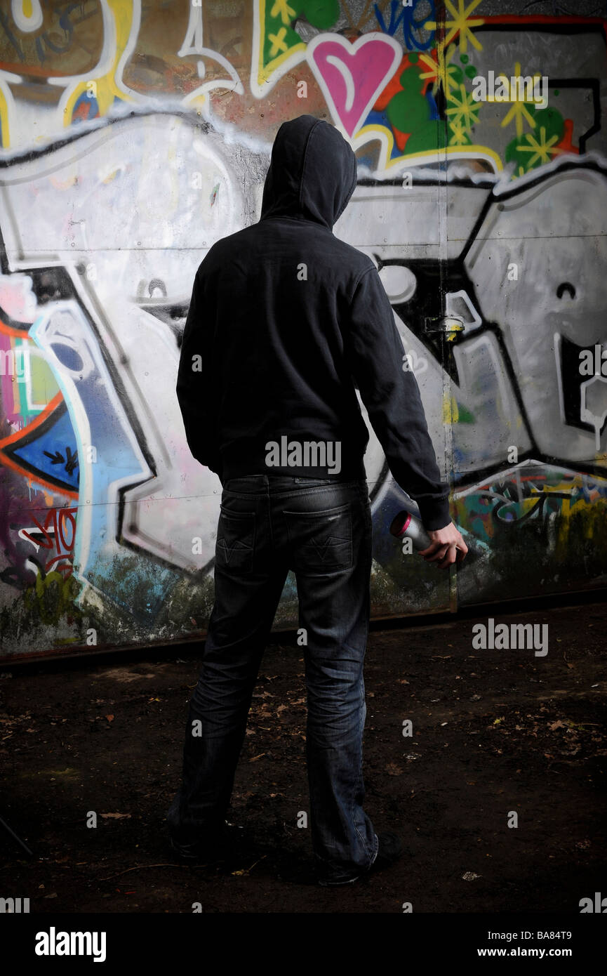 Person in dark clothing standing in front of a graffittied surface Stock Photo