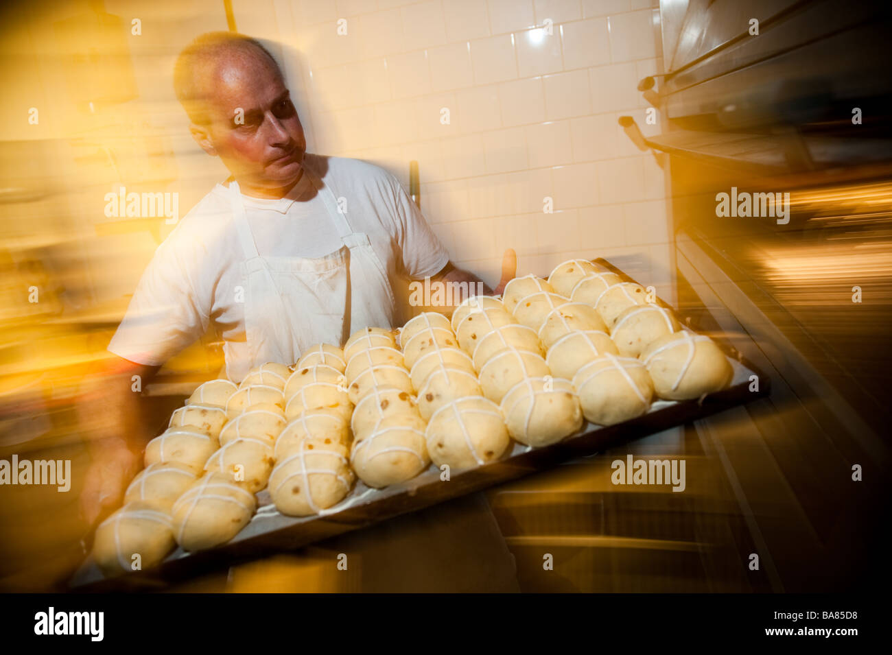 A baker preparing traditional hot cross buns for easter UK putting the raw uncooked buns into