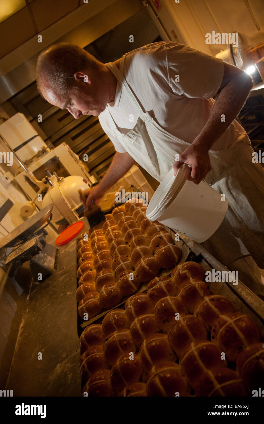 A baker making traditional hot cross buns for easter UK - applying glaze to the baked buns Stock Photo