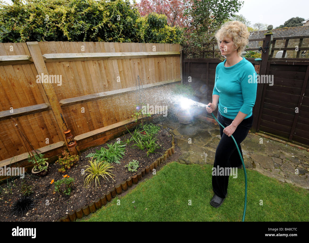 Blonde haired woman watering plants in her small town garden with garden light on Stock Photo