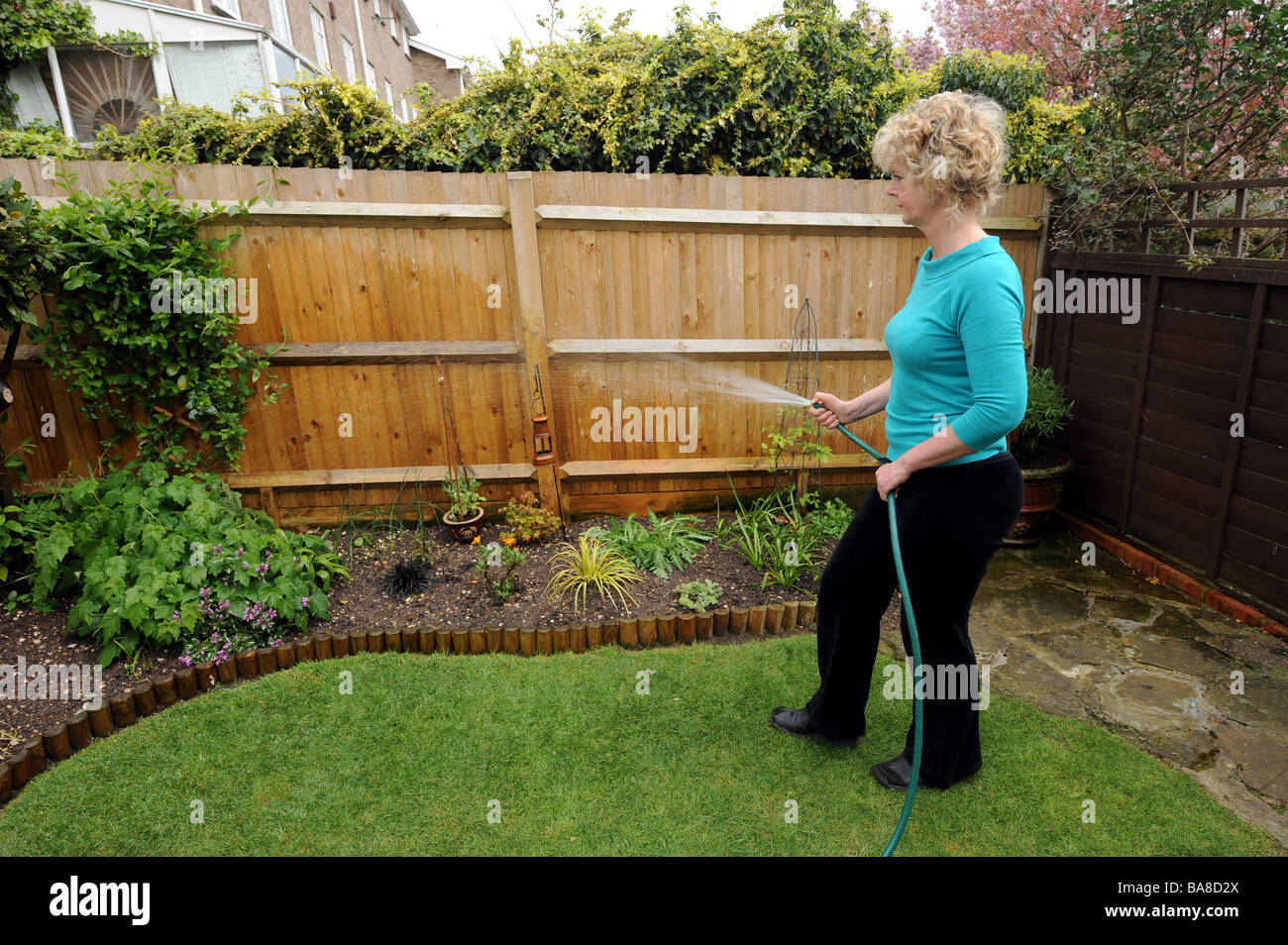 Blonde haired woman watering plants in her small town garden Stock Photo