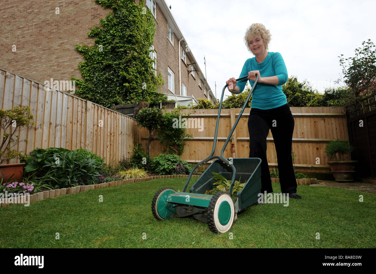 Woman Mowing The Grass Lawn In Small Town Garden Stock Photo