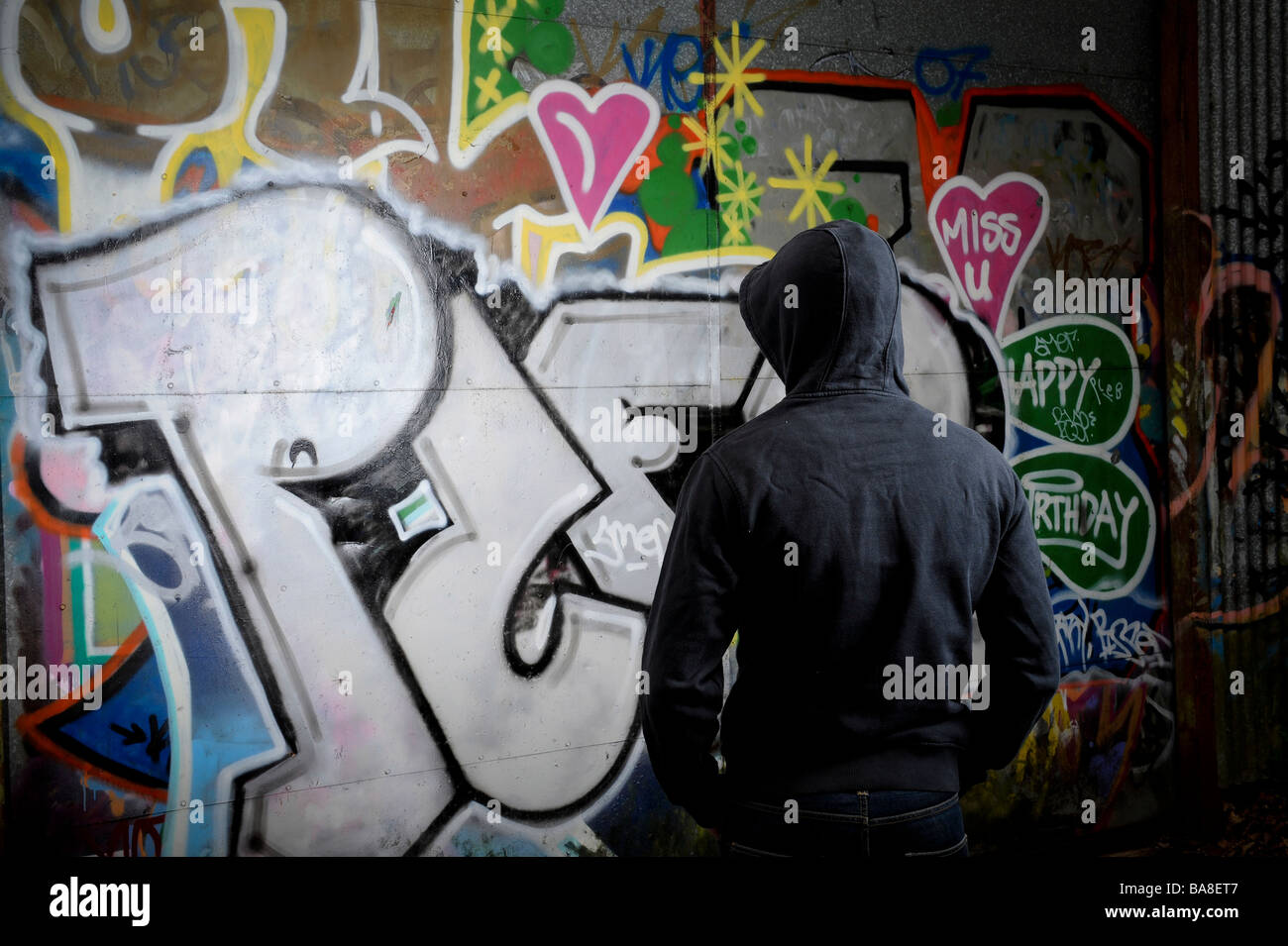 Person in dark clothing standing in front of a graffittied surface Stock Photo