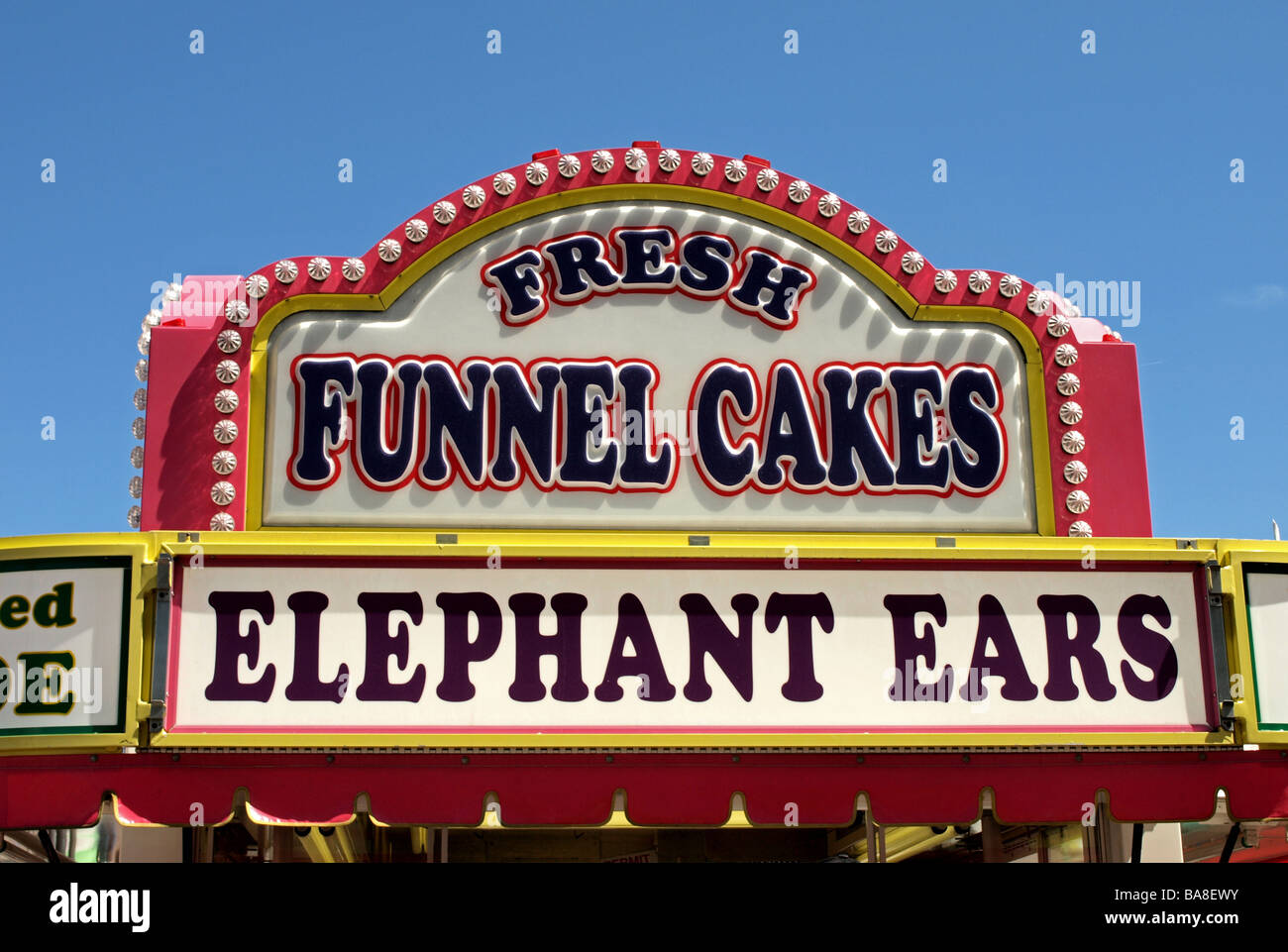carnival festival food signs for fast food including elephant ears and funnel cakes, blue sky and bright pink framing Stock Photo