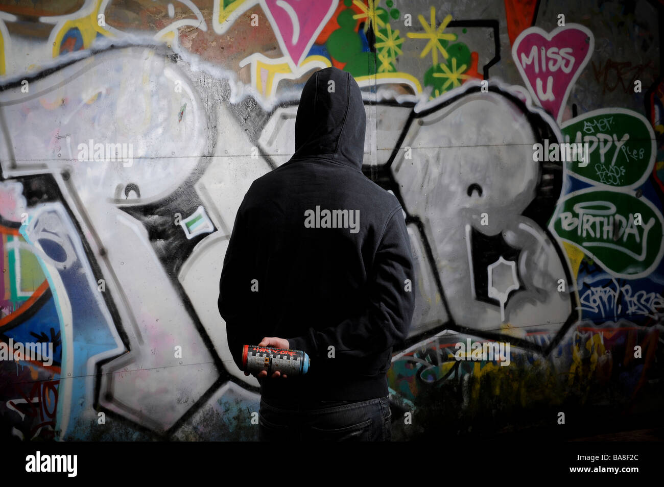 Person in dark clothing standing in front of a graffittied surface Stock Photo