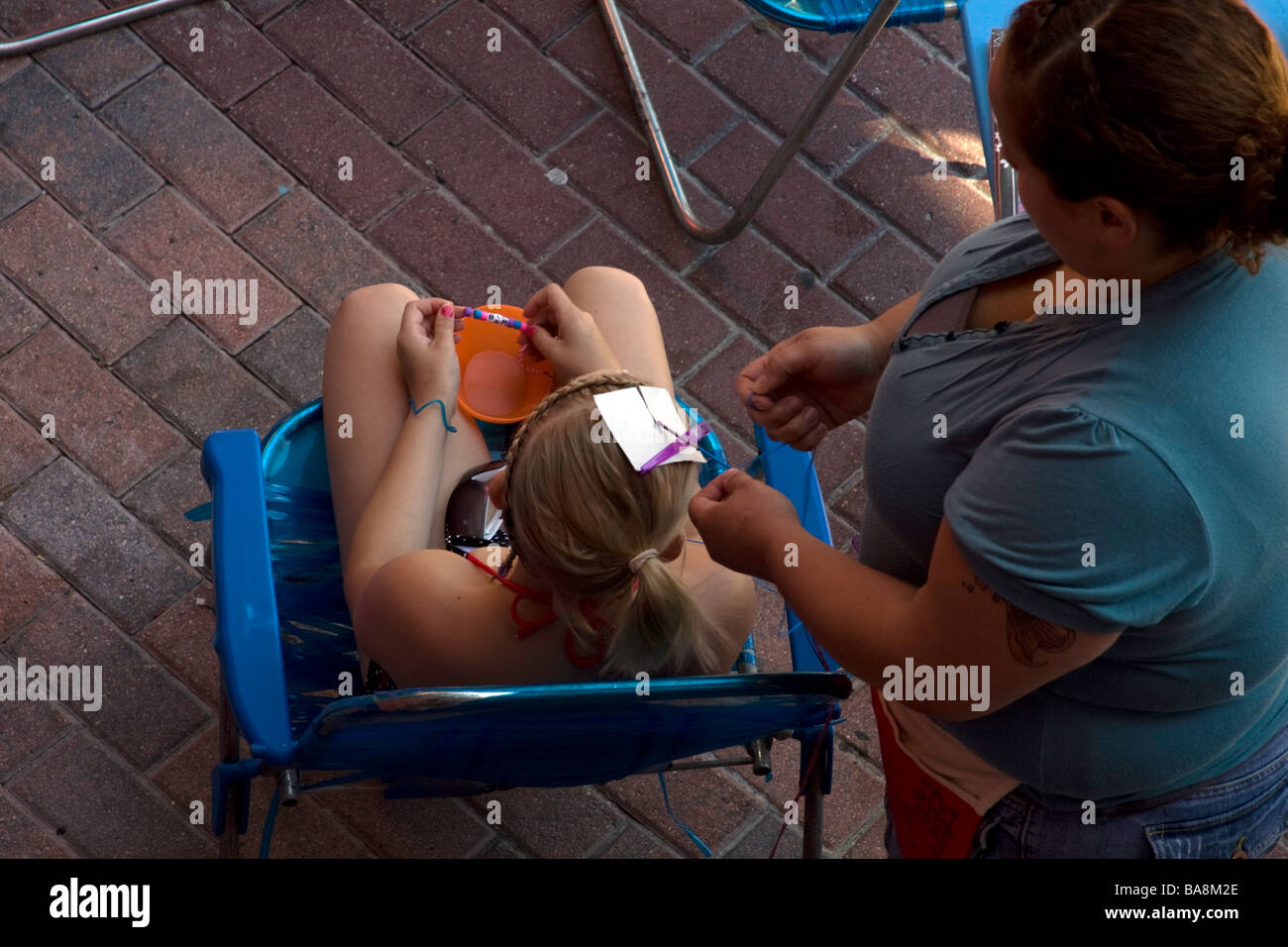 A toursit gets her hair braided by a local worker during spring break while sitting in a chair. Stock Photo
