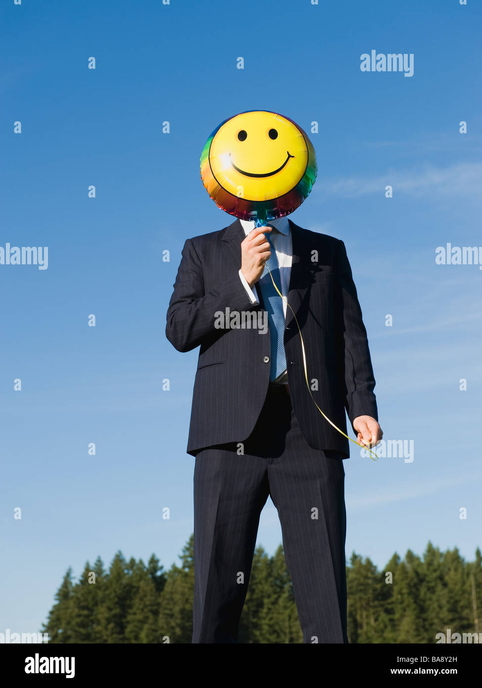 Businessman holding smiley face balloon over face Stock Photo